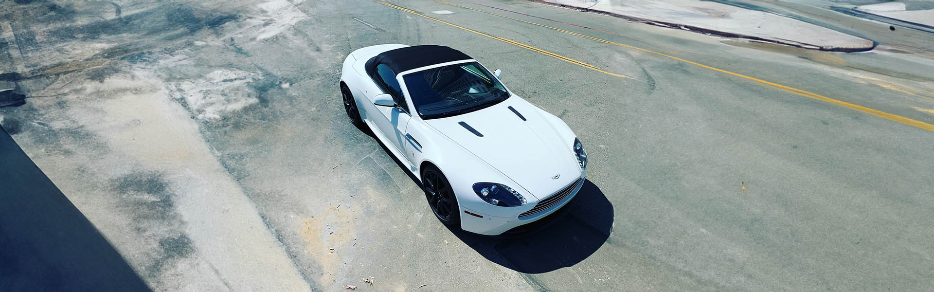 Aerial view of a white Aston Martin convertible on an open road, symbolizing freedom and style offered by Icon Servicing.