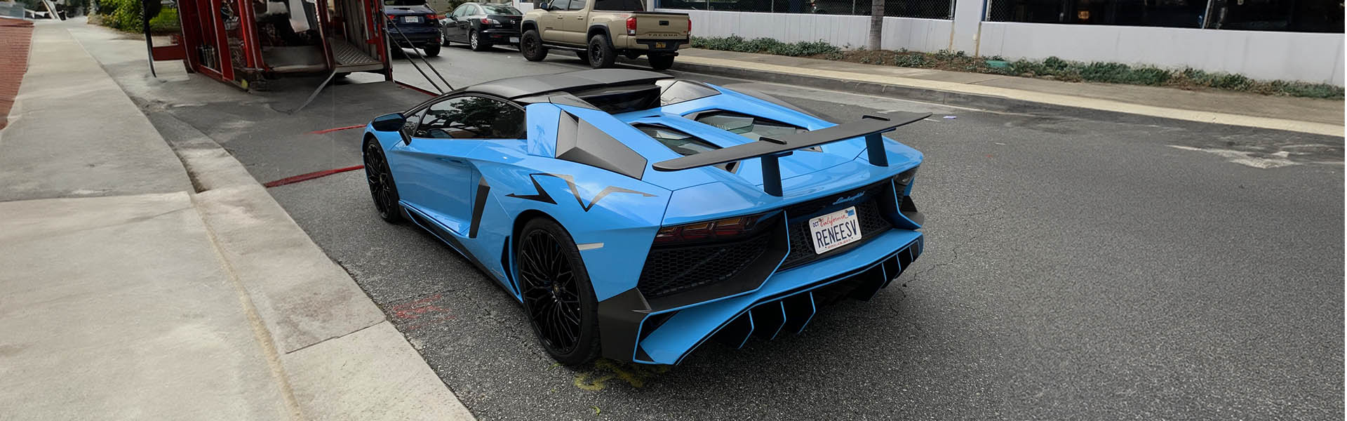 Rear view of a bright blue Lamborghini Aventador on a city street, showcasing the powerful and exotic vehicles available at Icon Servicing.