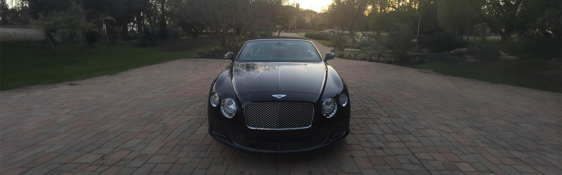 A sophisticated black Bentley parked in a scenic driveway, showcasing the refined and luxurious vehicles offered at Icon Servicing.
